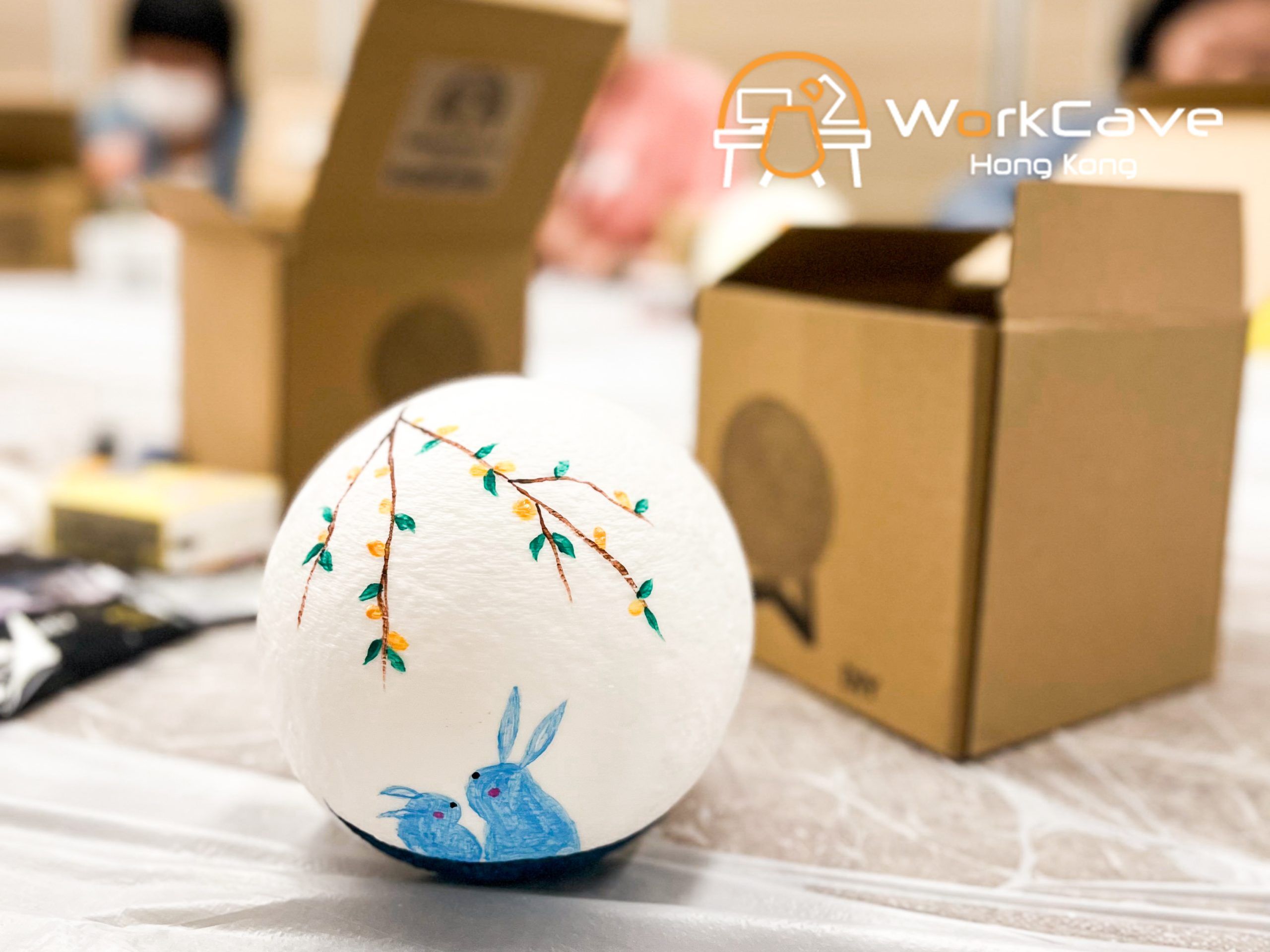 A close up to one of the moon lamps painted two blue rabbits looking at each other under a tangerine tree