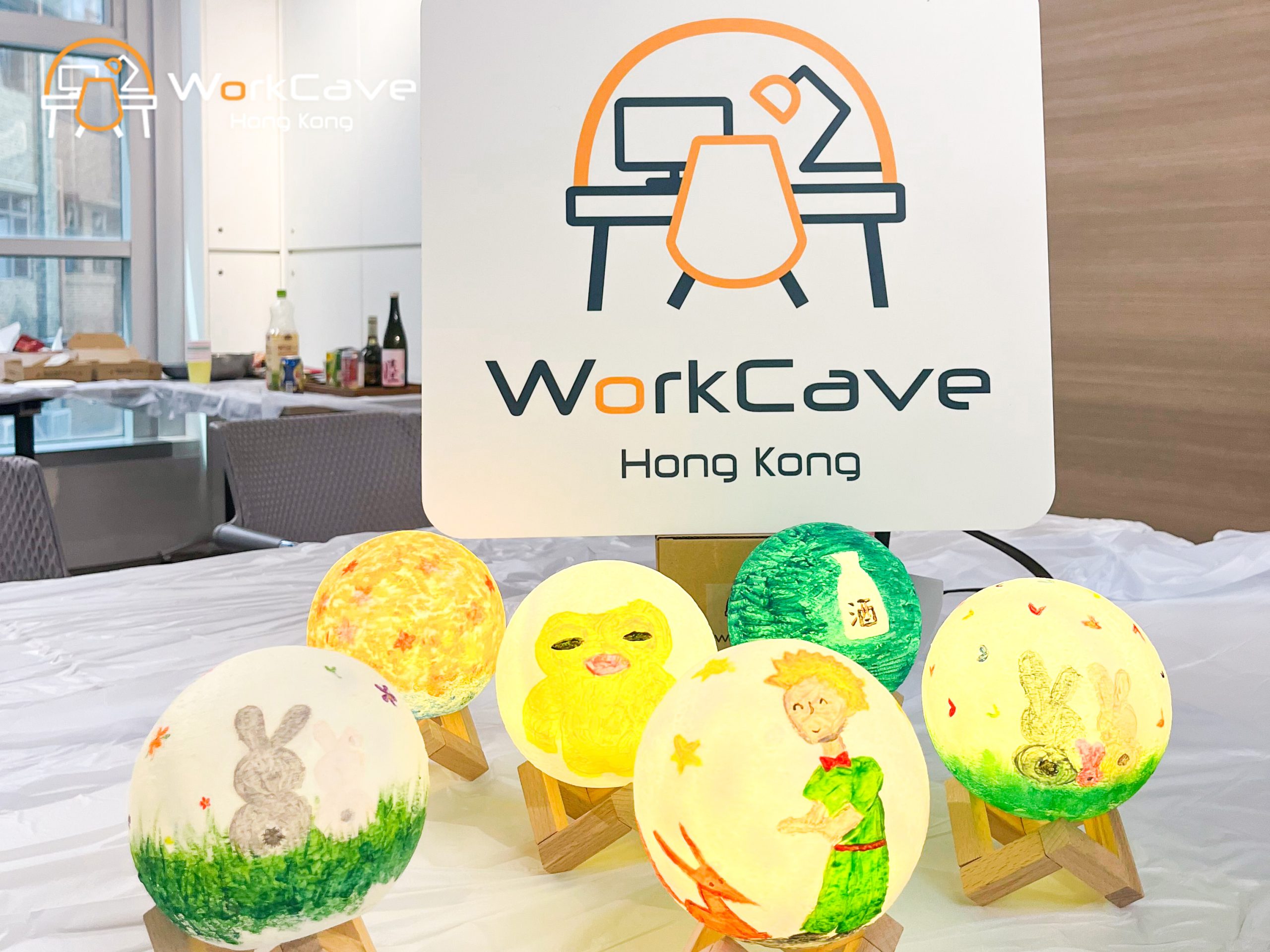 Seven glowing circle lamps painted the little prince, flowers, rabbits, wine etc. in front of the WorkCave logo foamboard
